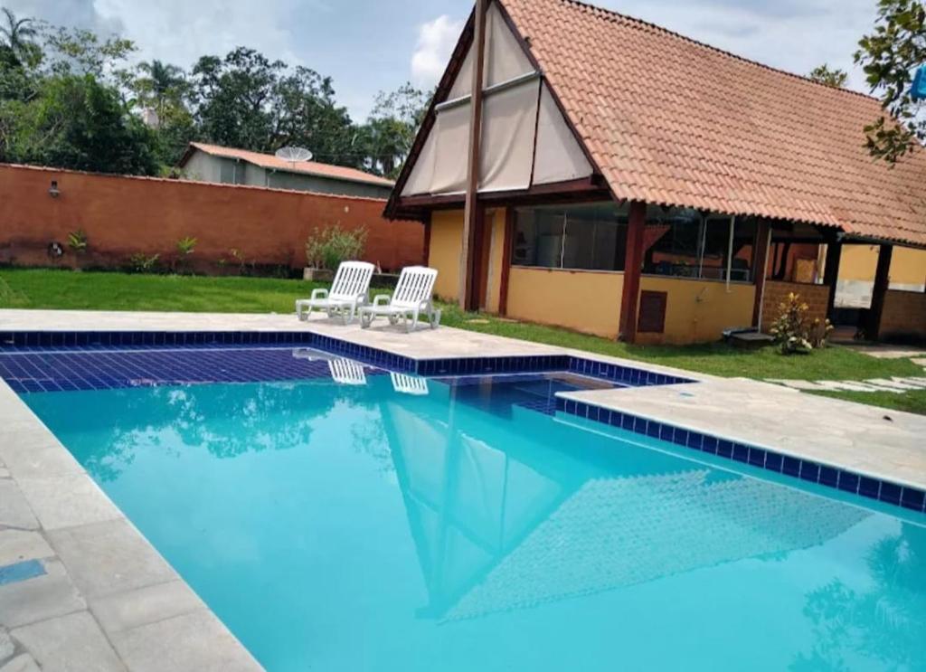 a swimming pool with two chairs and a house at Recanto Rocas in Pirenópolis