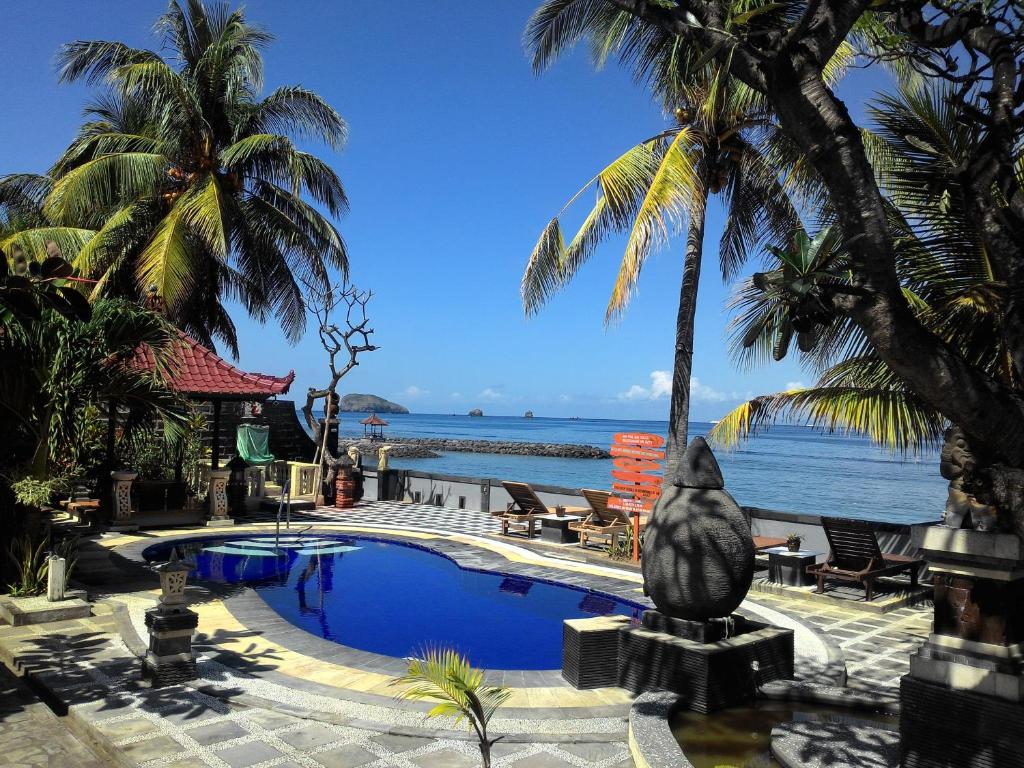 a resort swimming pool with palm trees and the ocean at Segara Wangi Beach Cottages in Candidasa