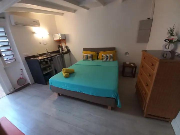 a bedroom with a blue bed and a kitchen at Chez Anne - Aux Délices de Maurice in Saint Martin