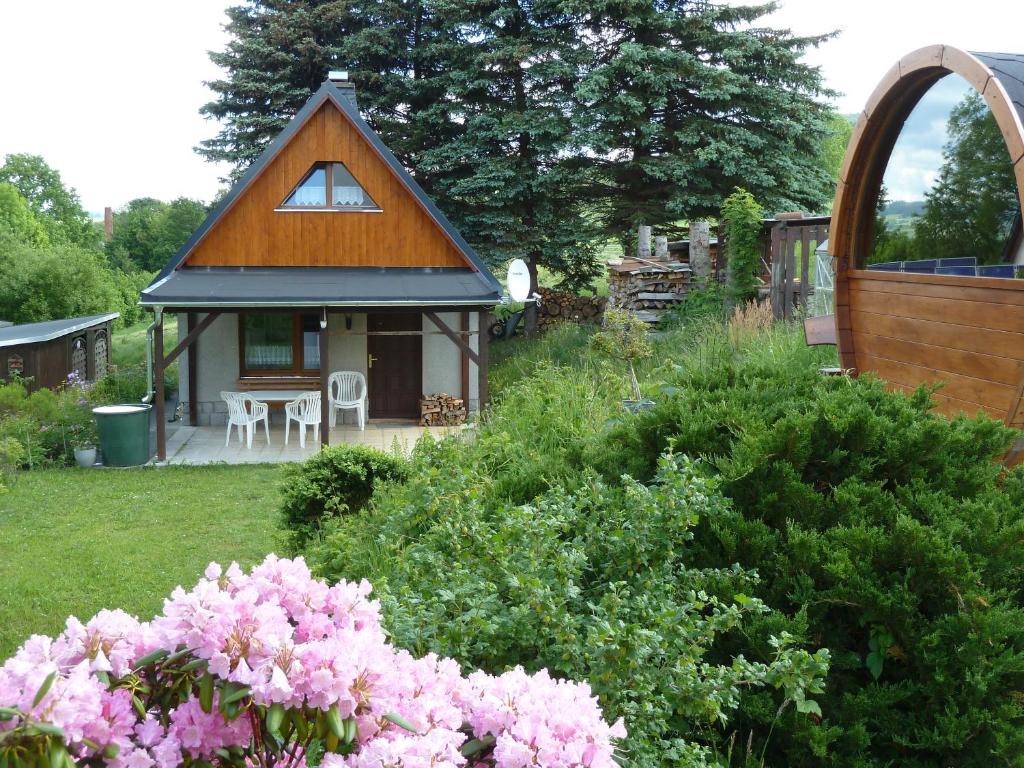 ein kleines Haus in einem Hof mit rosa Blumen in der Unterkunft Ferienhaus mit Kamin , Terrasse und Aussensauna in Pöhla