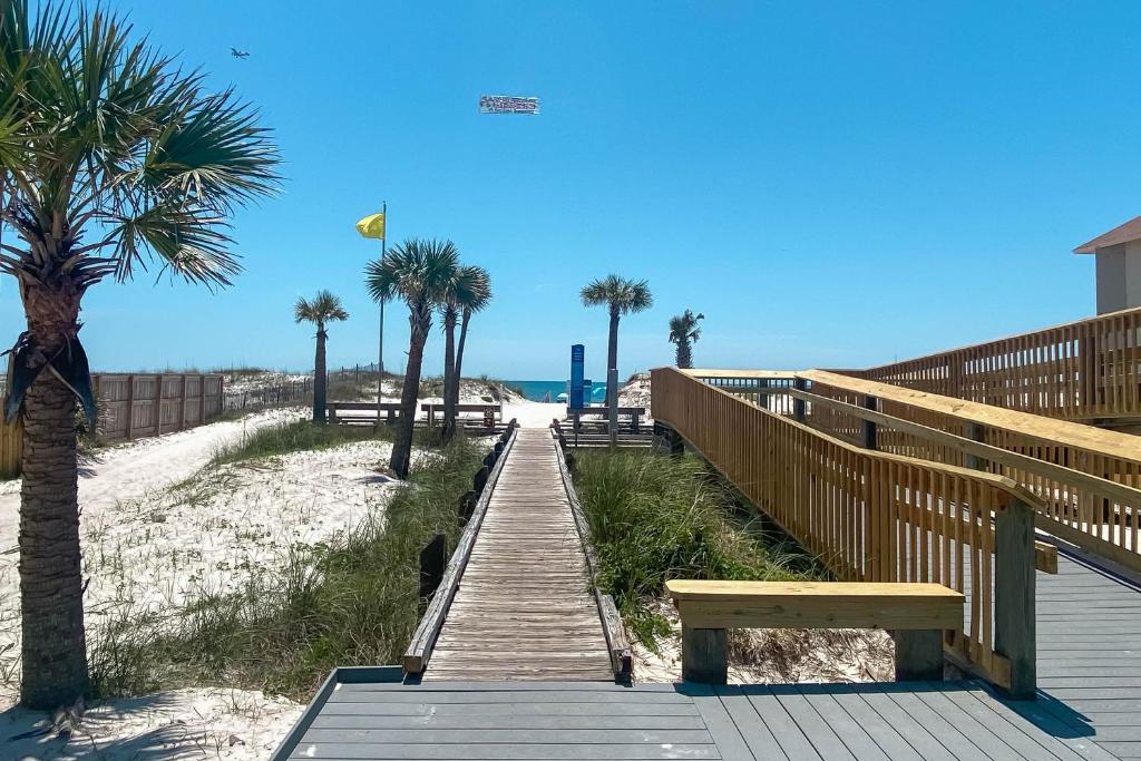 a wooden boardwalk to the beach with palm trees and a bench at Paradise Isle 34 in Gulf Shores