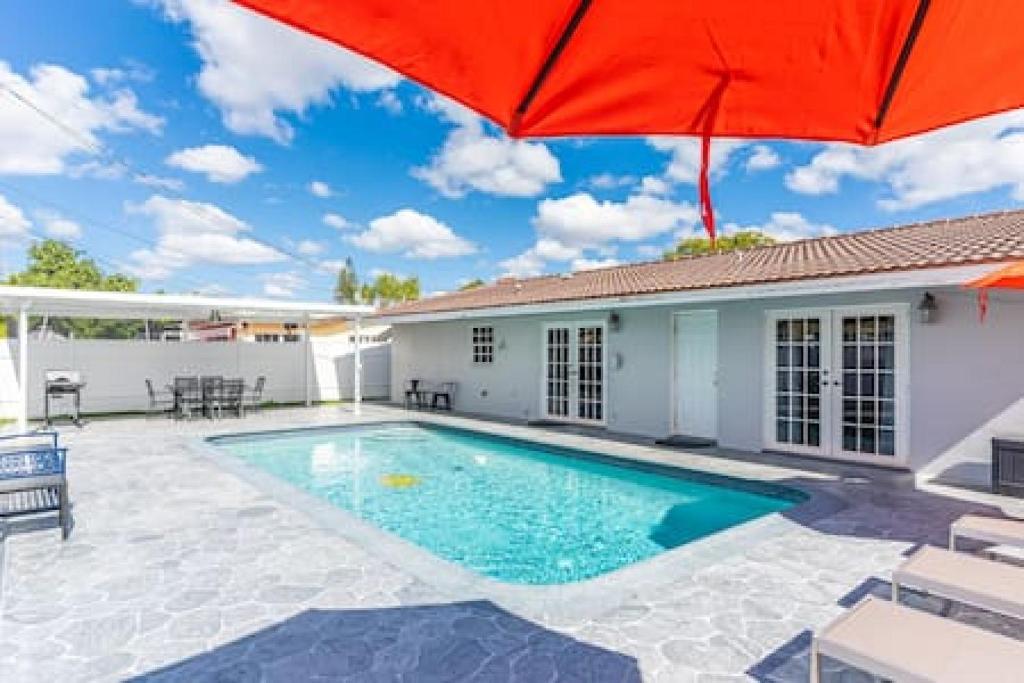 a house with a swimming pool and a red umbrella at Serene Poolside Getaway in Miami Gardens