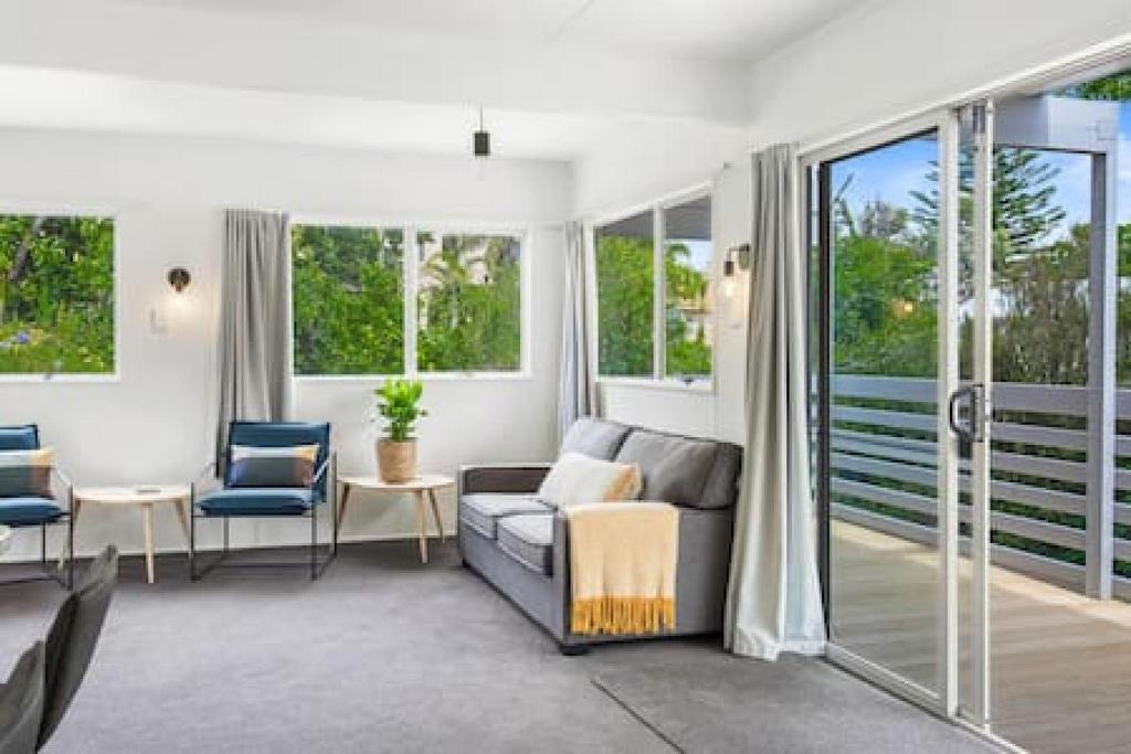 een woonkamer met een bank, stoelen en ramen bij Cockle Bay Getaway is close to beach in Auckland