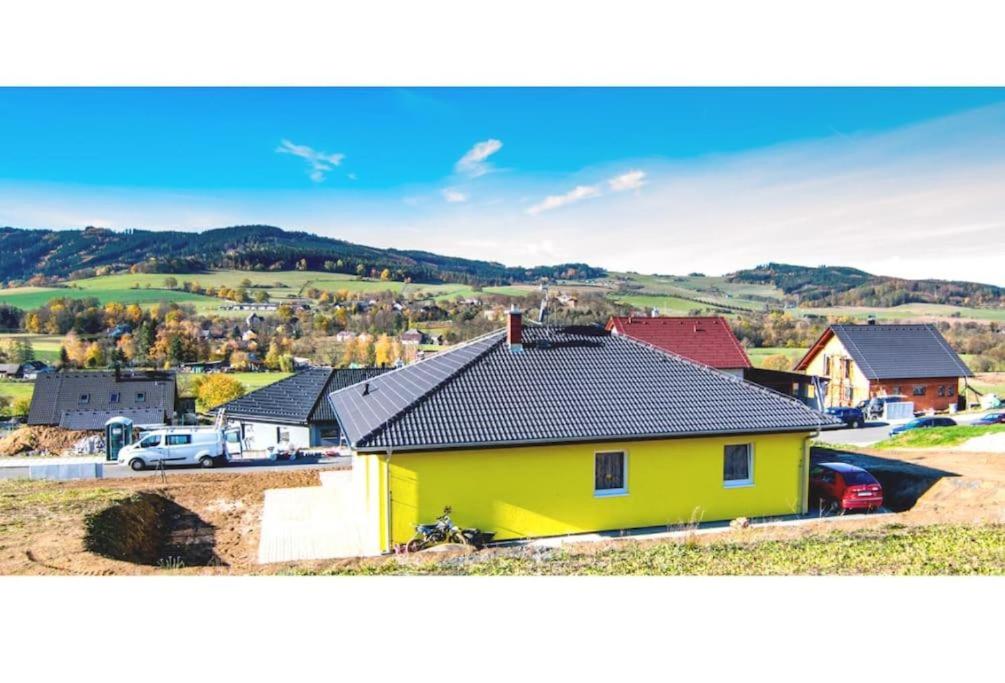 a yellow house with a black roof in a town at Šumava U Janiny in Strážov