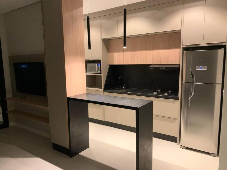 a kitchen with a black counter and a refrigerator at Apto inteiro 2 quartos, condomínio com piscina aquecida in Bombinhas