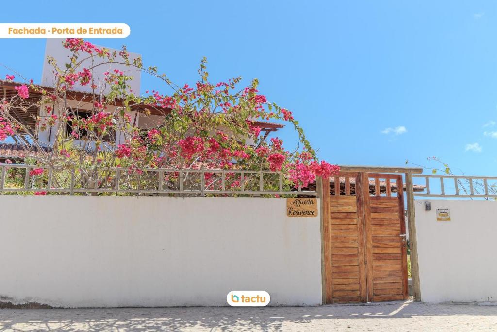 un mur blanc avec une porte en bois et des fleurs roses dans l'établissement Apto térreo no Pontal do Maceió Tactu, à Maceió