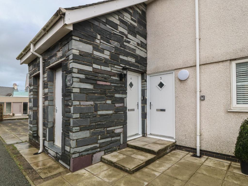 a house with a stone wall and a white door at Y Enciliad in Rhosneigr