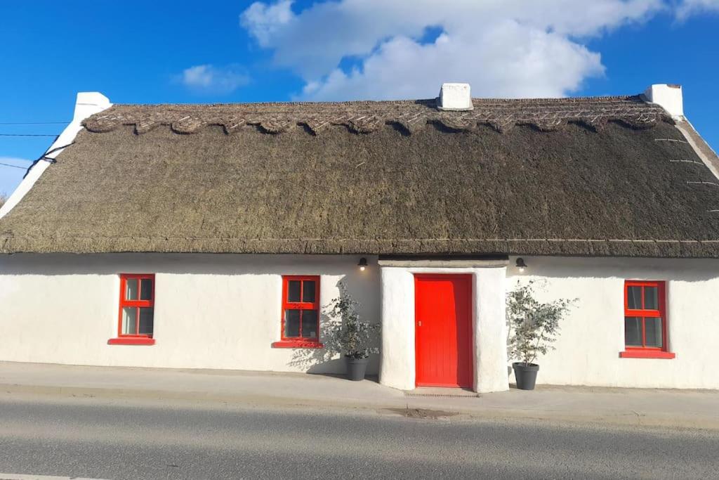 a white house with red doors and a thatched roof at Luxury 300yr old Irish thatch cottage close to sea in Rush