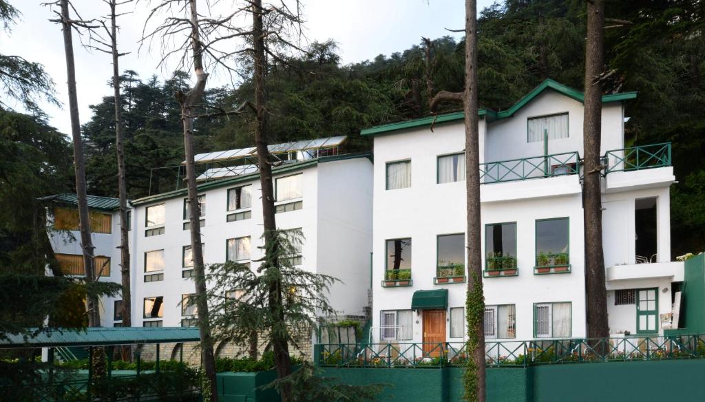 un edificio blanco con árboles delante de él en Honeymoon Inn Shimla en Shimla