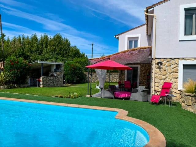 - une piscine en face d'une maison avec un parasol rouge dans l'établissement Maison familiale à caumont sur durance, à Caumont-sur-Durance