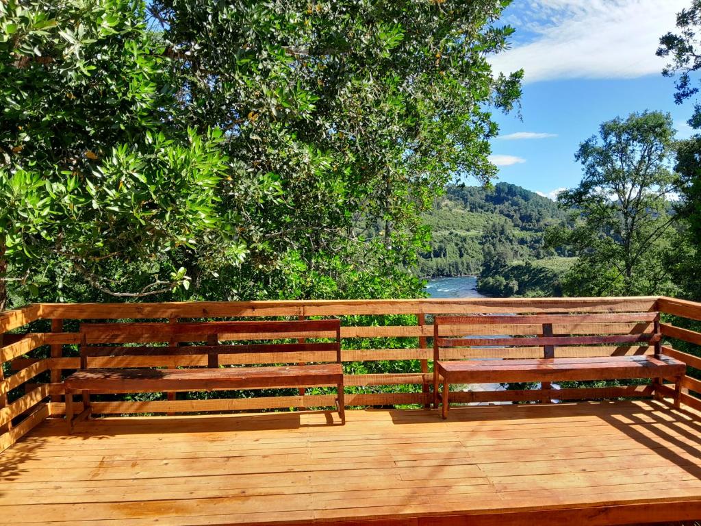two wooden benches sitting on a deck with a view of a river at El Arrayán in Lago Ranco