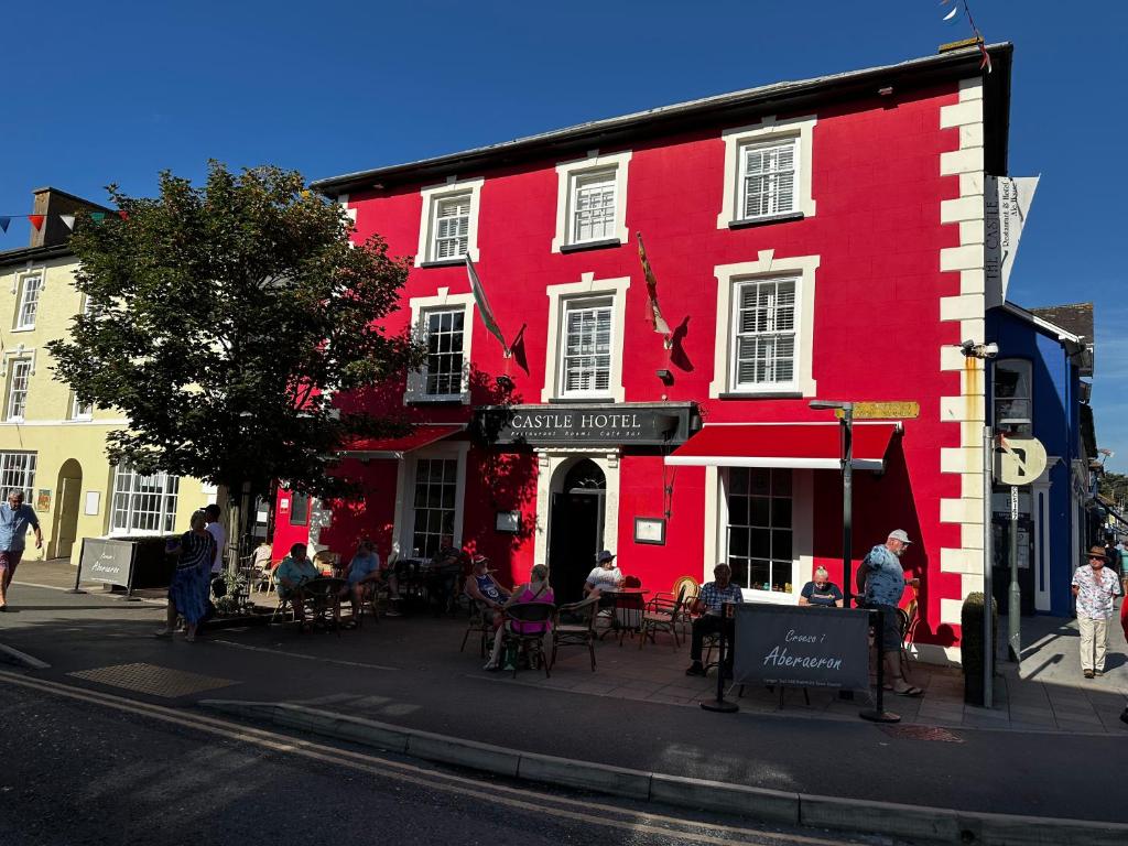 um edifício vermelho com pessoas sentadas fora dele em Castle Hotel em Aberaeron