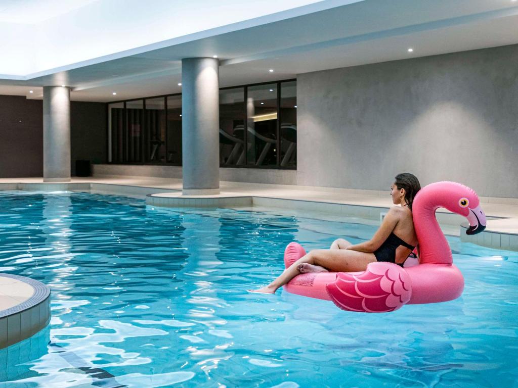 une femme assise sur un flamingo rose dans une piscine dans l'établissement Pullman Paris Roissy Cdg Airport, à Roissy-en-France