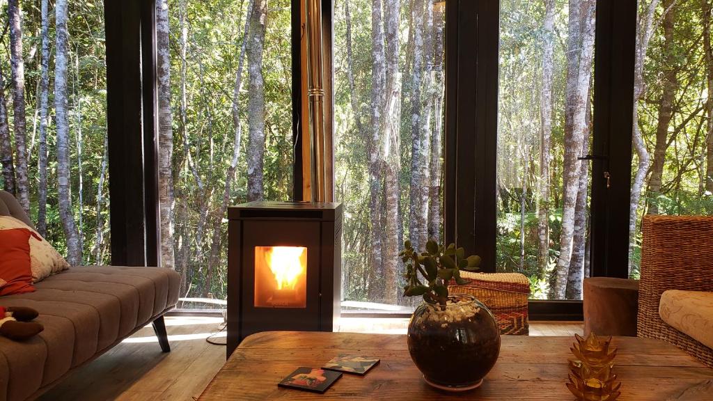 a living room with a fireplace in front of trees at Cabaña Bosque Rio in Puerto Varas