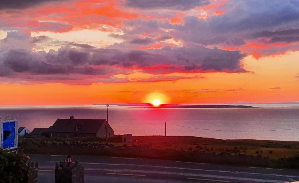 a sunset over the ocean with a house in the foreground at The Ramblers Rest B&B in Doolin