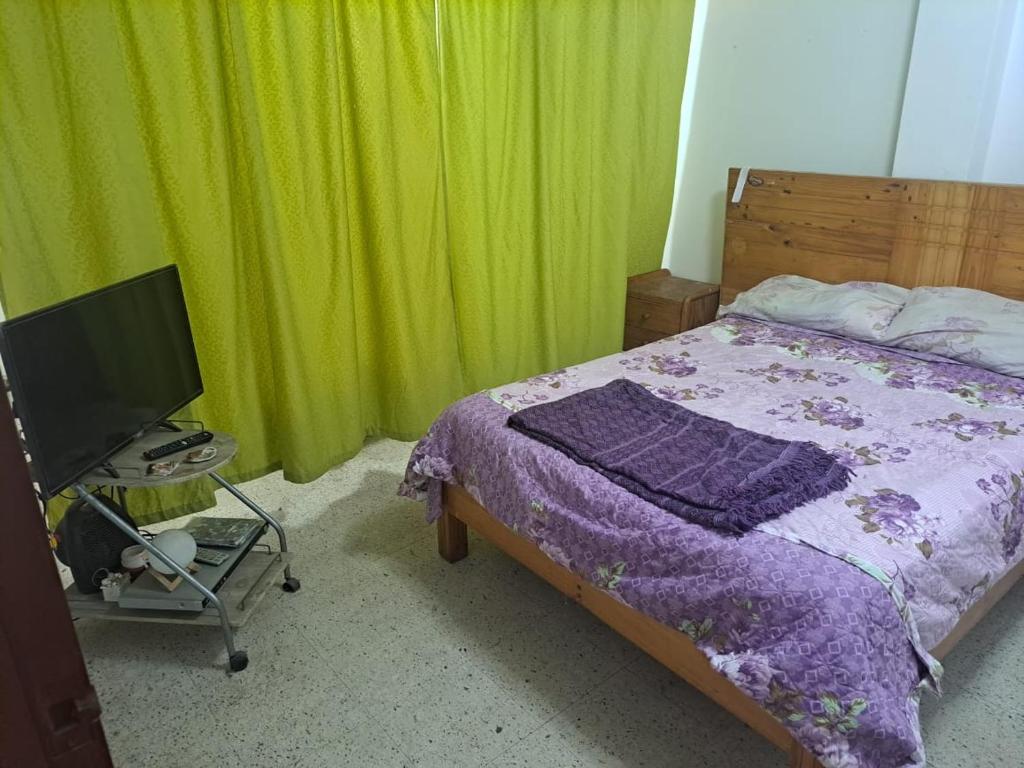 1 dormitorio con cama, TV y cortinas verdes en Sientete en casa, en Ilo