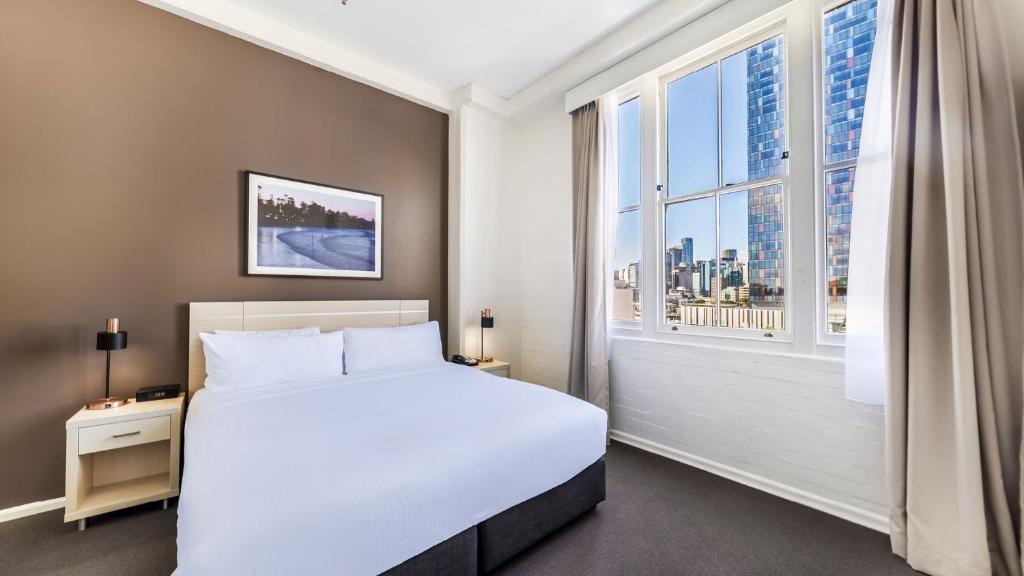 um quarto com uma cama branca e uma grande janela em Oaks Sydney Goldsbrough Suites em Sydney