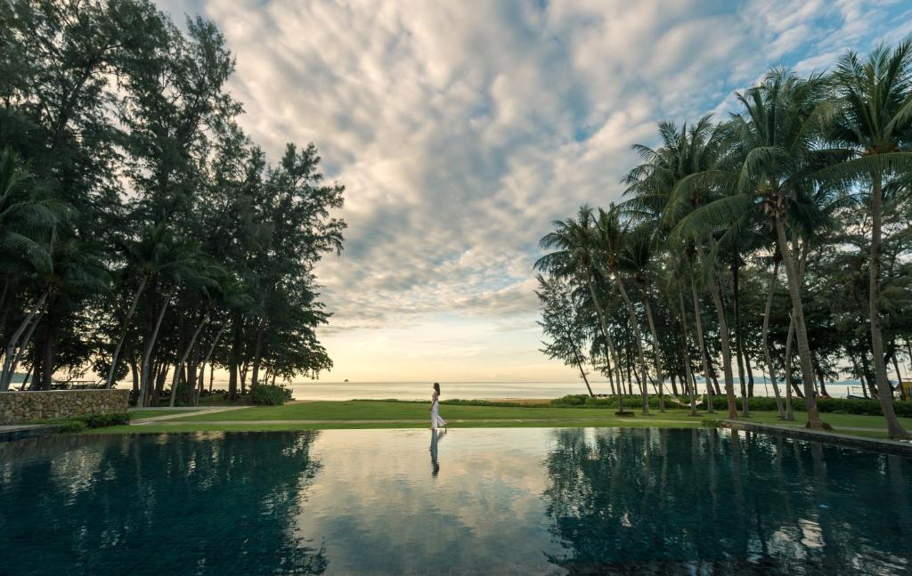 a person standing in the water next to a swimming pool at Dusit Thani Krabi Beach Resort - SHA Extra Plus in Klong Muang Beach