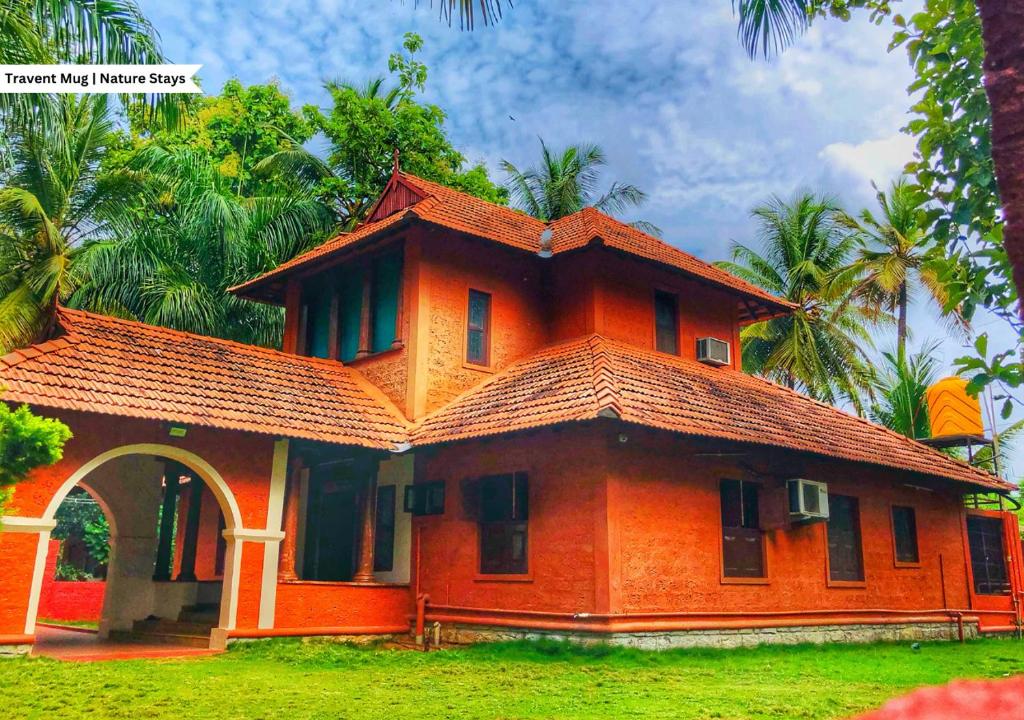 ein orangenes Haus mit einem Dach darüber in der Unterkunft Ambara Kovilakam Private Pool Villa by Travent Mug in Rāmanagaram