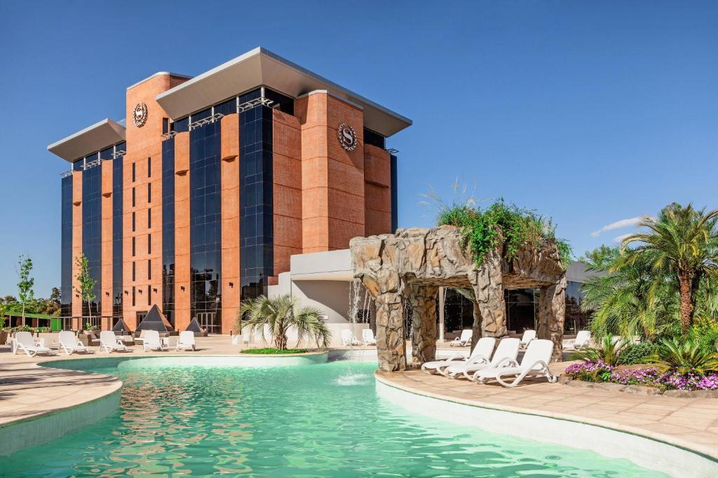 a resort with a pool and chairs and a building at Sheraton Tucumán Hotel in San Miguel de Tucumán