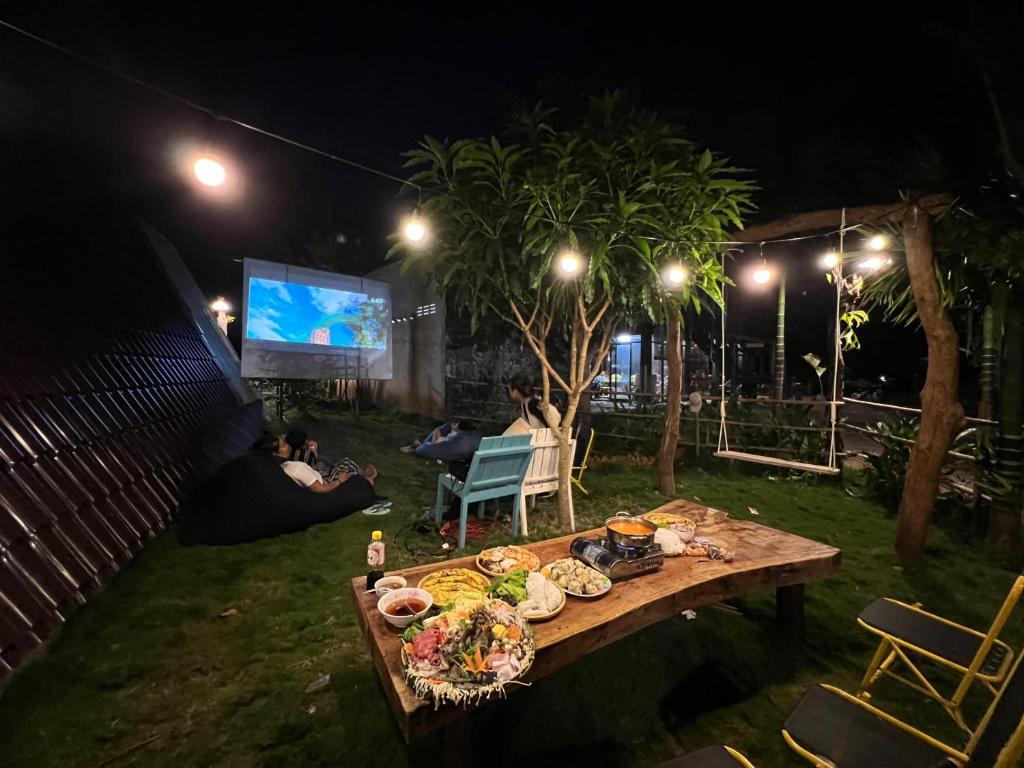 una mesa con comida y gente mirando una pantalla por la noche en Sunflower Garden 