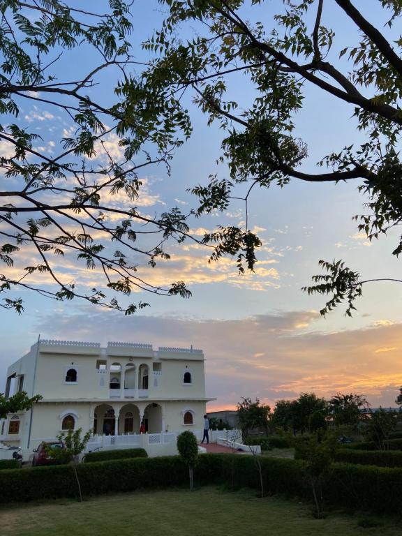 a white building with a sunset in the background at Dera Padlia - A Rural Experience Farm Stay 