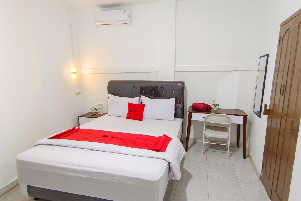 Schlafzimmer mit einem weißen Bett mit roter Bettwäsche und einem Schreibtisch in der Unterkunft RedDoorz at Kubu Selem Lampung in Bandar Lampung
