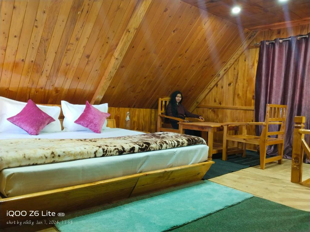 uma mulher sentada numa mesa num quarto com uma cama em Forest View Cottage em Jibhi