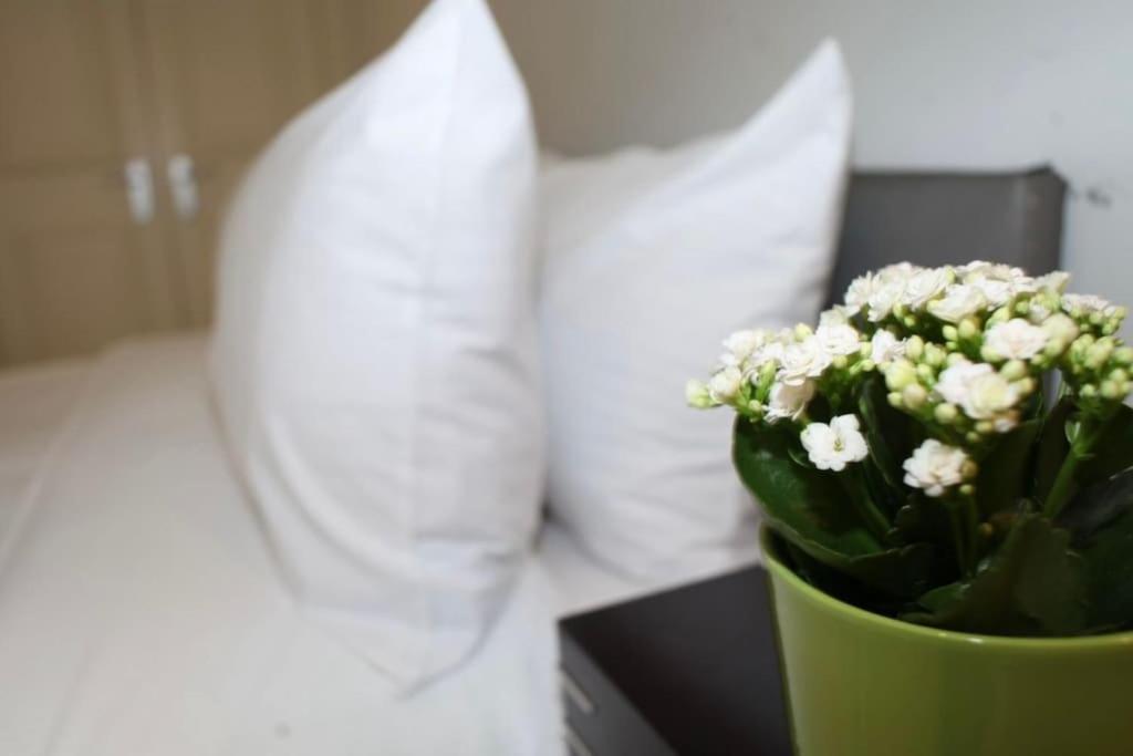 a green vase with white flowers in front of a bed at 2 Bed Flat South Kensington in London