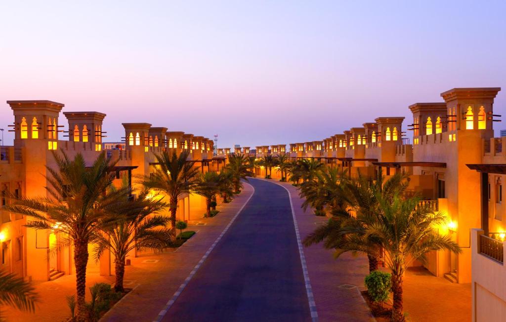 een straat met palmbomen en gebouwen 's nachts bij Al Hamra Village Hotel in Ras al Khaimah