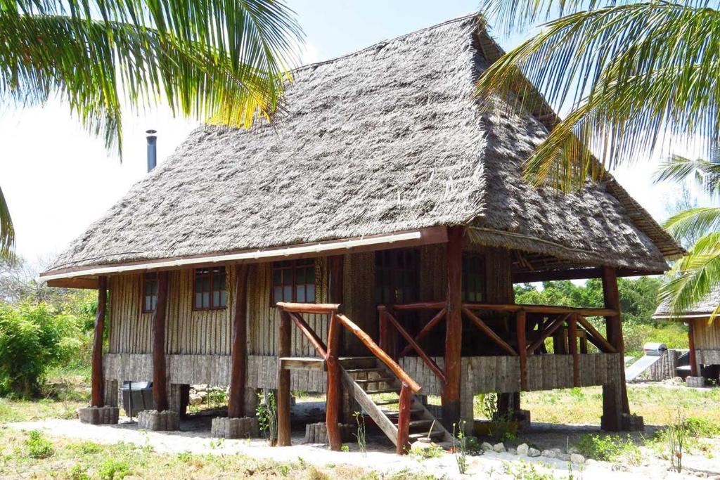 uma pequena casa com um telhado de palha e uma palmeira em Pemba Eco Lodge em Kengeja