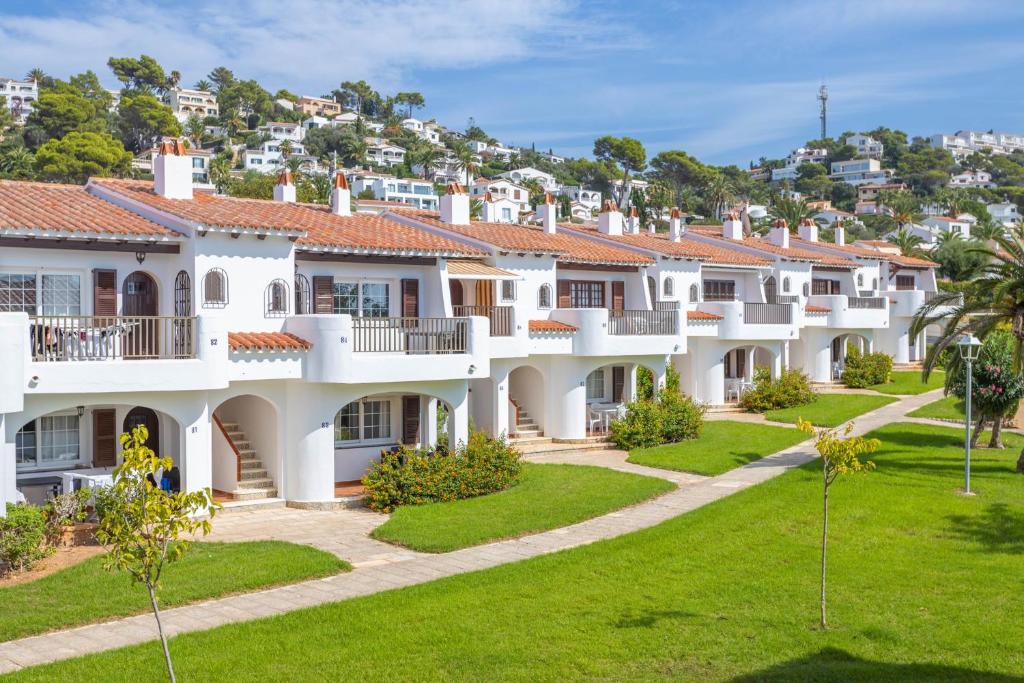 una fila di case bianche con una collina sullo sfondo di Apartamentos Son Bou Gardens By MENORCARENTALS a Son Bou