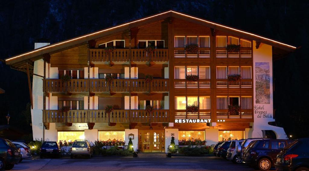 een groot houten gebouw met een balkon op een parkeerplaats bij Hotel Crepes de Sela in Campitello di Fassa