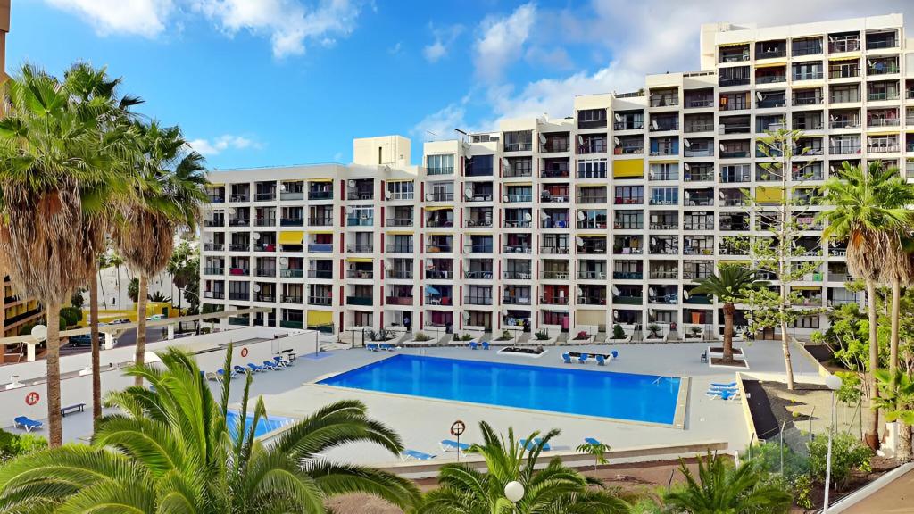 a large hotel with a pool and palm trees at Blanco&Azul - Ocean View Balcony, Pool and Perfect Location in Playa de las Americas