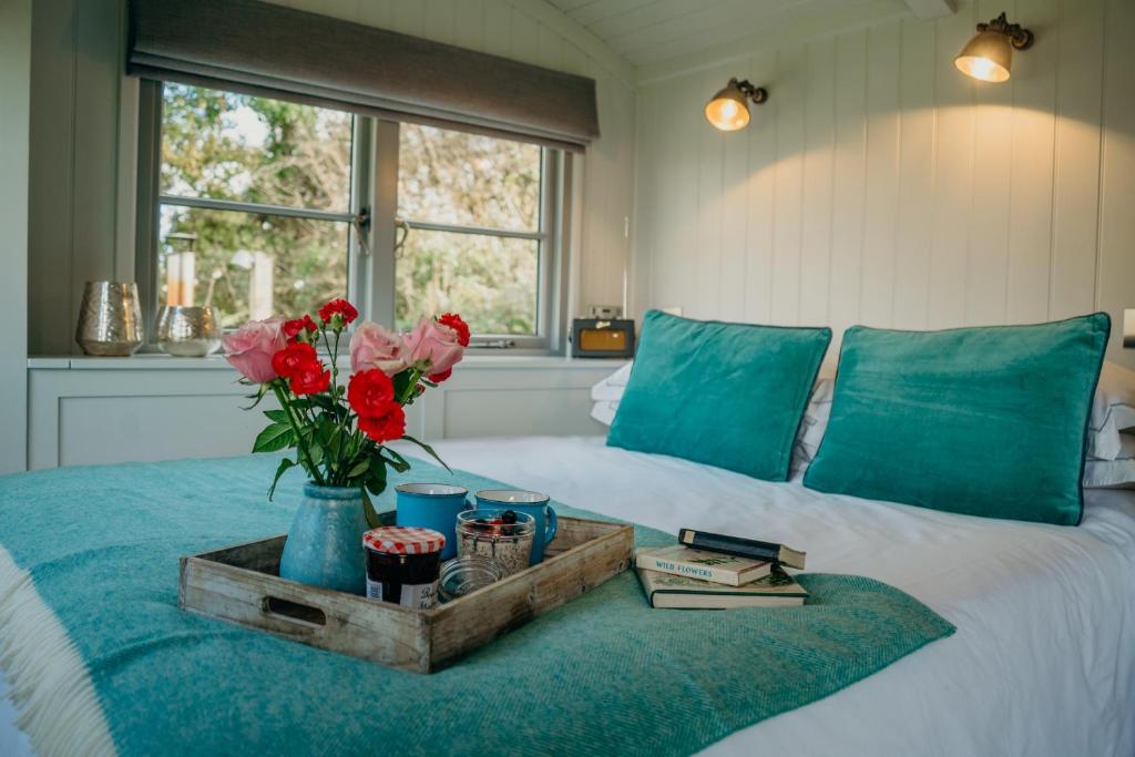 een bed met een dienblad met bloemen en boeken erop bij Blatchford Briar - Award Winning Private Shephards Huts with their own Secluded Hot Tubs in Milton Abbot