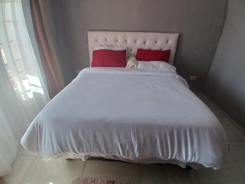 a white bed with two red pillows on it at Partulaka Rest Inn in Maun