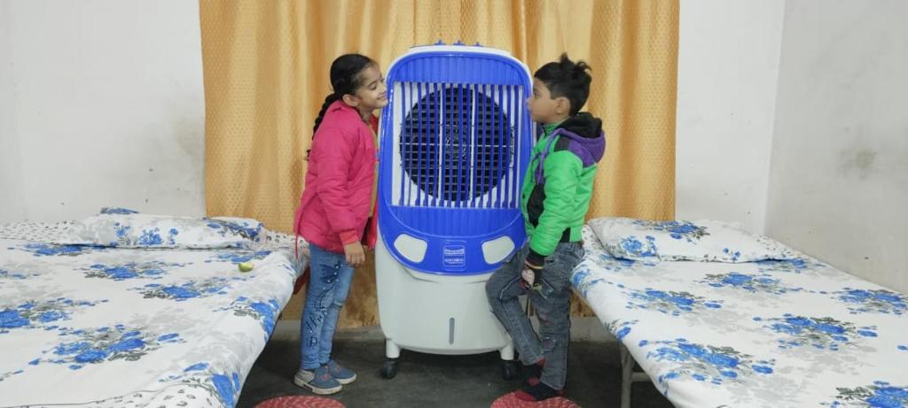 two children are standing in a room with a blue cage at Mannat Rooms in Allahābād