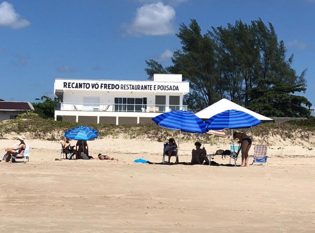 eine Gruppe von Menschen, die unter Sonnenschirmen am Strand sitzen in der Unterkunft Pousada Recanto Vô Fredo in Guaratuba