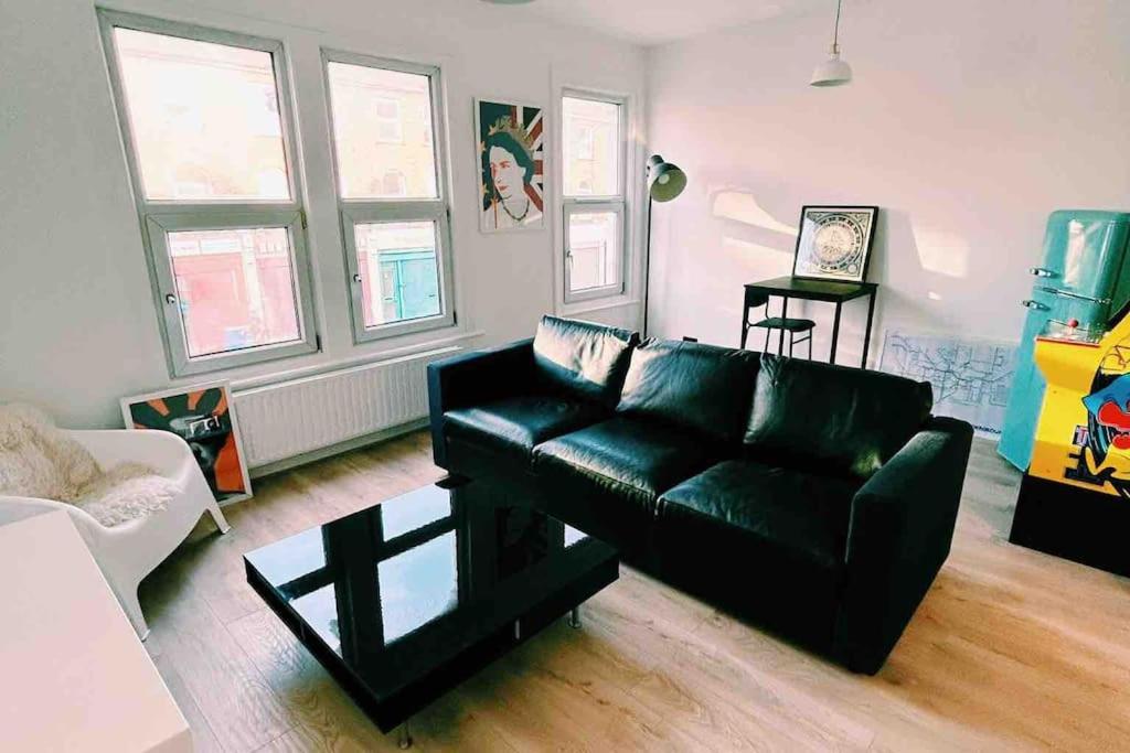 sala de estar con sofá de cuero negro y ventanas en London Flat next to Central Line Underground Station, en Londres