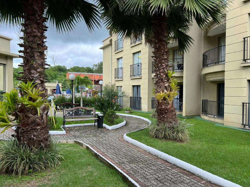 una pasarela entre dos edificios de apartamentos con palmeras en Aldeia das Águas Park Resort - Quartier - Flat B102 en Barra do Piraí