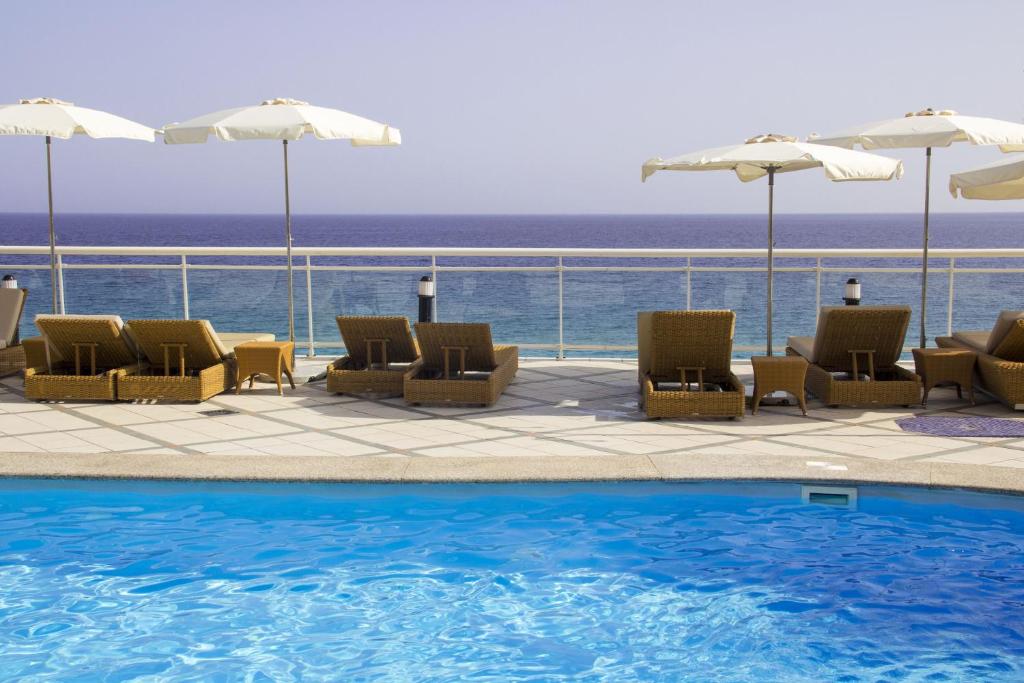 a pool with chairs and umbrellas next to the ocean at XQ El Palacete in Morro del Jable