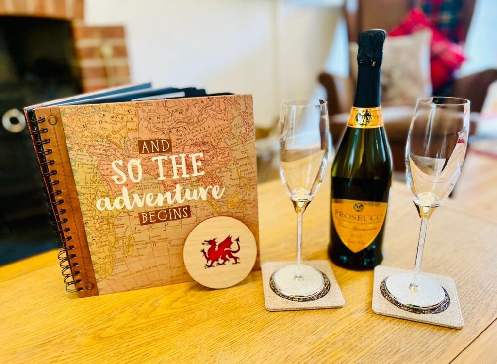 a book and two glasses on a table with a bottle of wine at Gorwel, Spacious 3 Bedroom Cottage near the Beach in Llanarth