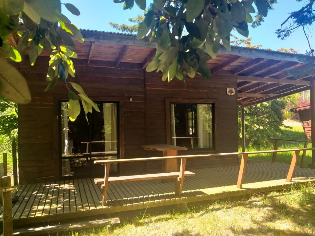 ein Blockhaus mit einer Veranda und einer Bank auf einem Deck in der Unterkunft Cabaña Río Iculpe in Lago Ranco