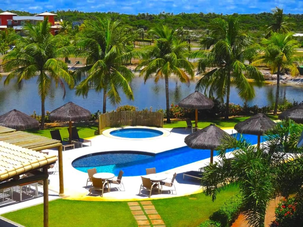 a resort pool with palm trees and a body of water at Condominio Iberostate in Praia do Forte