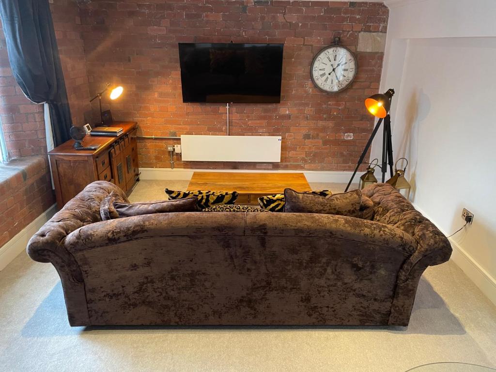 a couch in a living room with a clock on a brick wall at Staycation York at Cocoa Suites in York