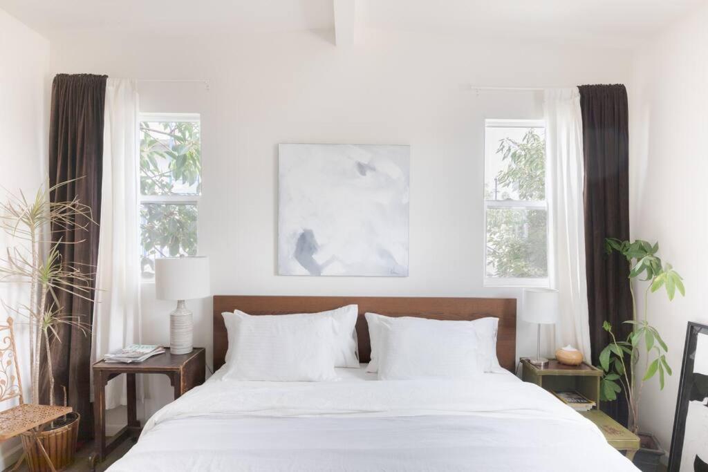 a bedroom with a white bed with two windows at Take it easy on the porch in a Hollywood hideaway in Los Angeles