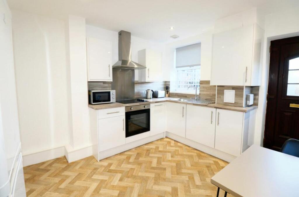 cocina con armarios blancos y suelo de madera en Orionn Place en Nottingham