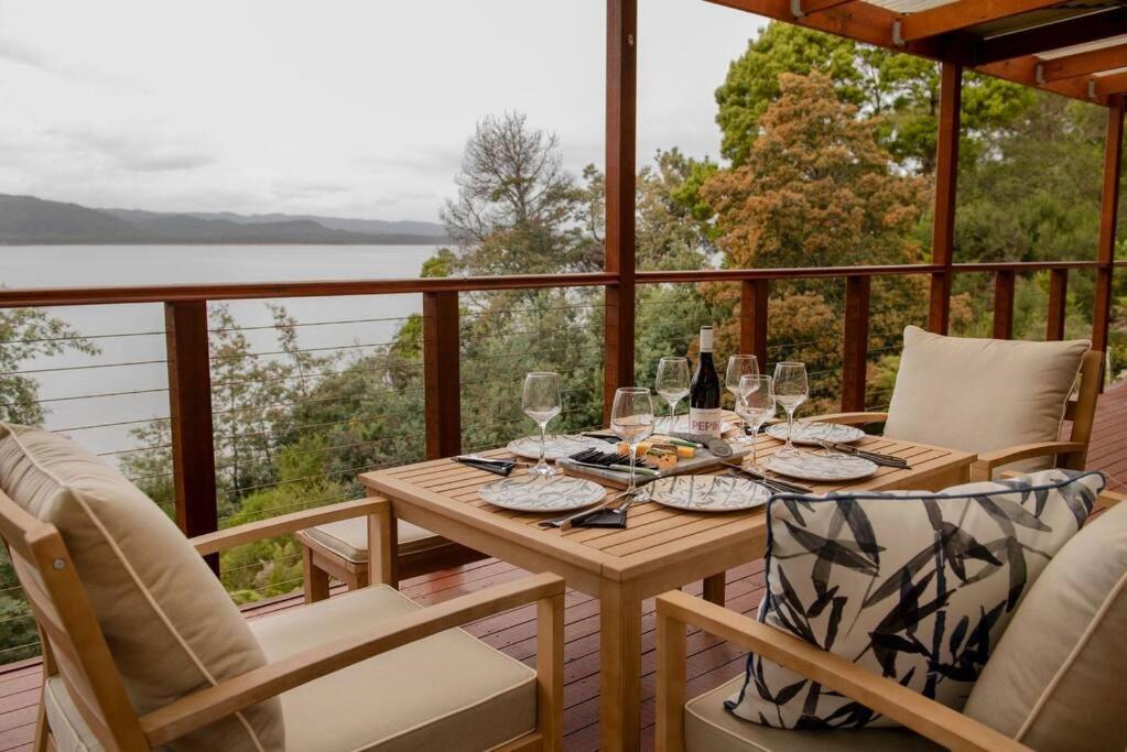 una mesa de madera con copas de vino en el balcón en Majestic 2 bedroom villa with panoramic bay views, en Strahan