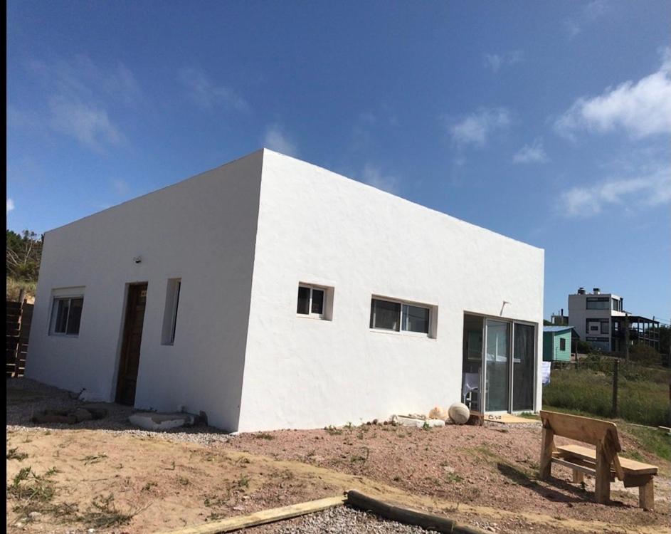 una casa blanca con un banco delante en Casa de Coral en Punta Del Diablo