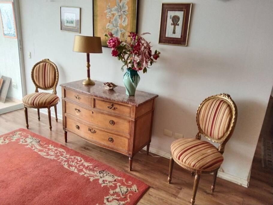 Dos sillas y un tocador con un jarrón de flores. en Departamento en Barrio Exclusivo - La Serena, en La Serena